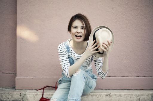 An attractive young female with a hat sitting on the sidewalk under the sunlight at daytime