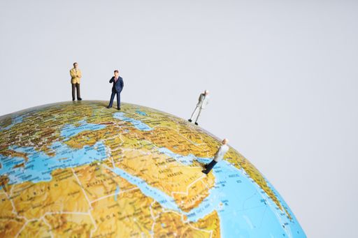 miniature business people stand spread out on a globe in different countries. White background