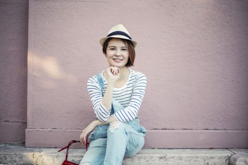 An attractive young female with a hat on sitting on the sidewalk under the sunlight at daytime