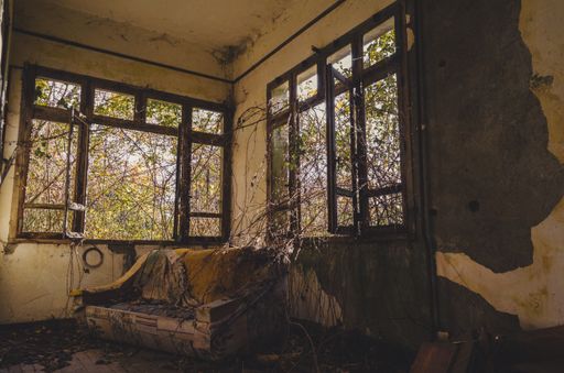 An old couch inside of a house with rusty walls and broken windows