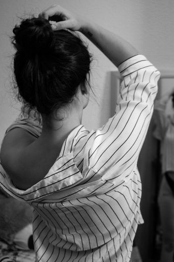 A vertical shot of the back of a young sexy woman wearing striped  shirt touching her hair with hands