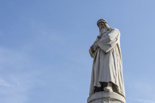 A low angle shot of a statue of Leonardo Da Vinci with a blue clear sky behind in Milan, Italy
