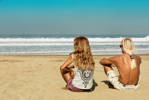 A back shot of a father and daughter sitting on the beach and looking at the pacific ocean, plage de Kuta, Bali