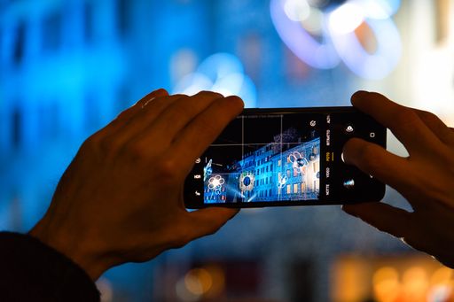 A hand shooting by a phone with colorful lights during the Lilu Light Festival in Lucerne at night