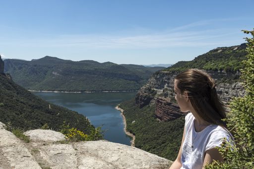 A young girl sitting in front of a beautiful natural landscape of a valley with a river. the girl is sitting looking at the landscape