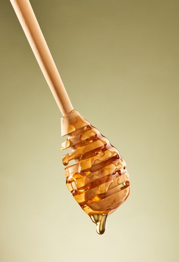 A closeup of honey flowing down the dipper on the blank green background