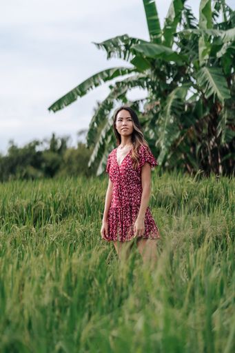 A vertical shot of an East Asian woman wearing a medical mask in an oat field in Bali, Indonesia.