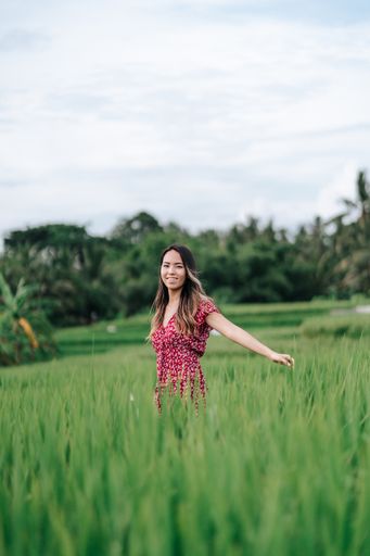 A vertical shot of an Asian Chinese woman standing in an oat field in Bali, Indonesia.