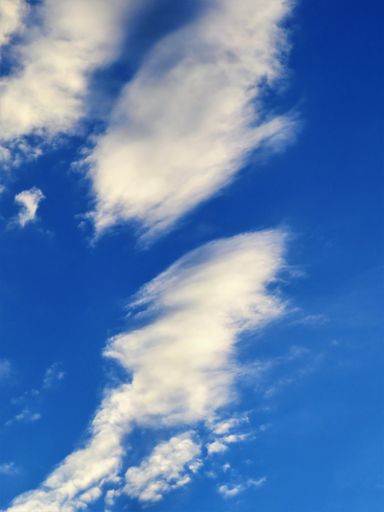 A vertical low angle shot of the beautiful fluffy clouds in the blue sky