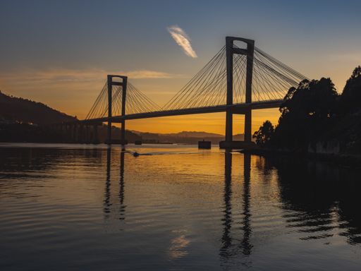 A silhouette of a bridge over a river at golden sunset