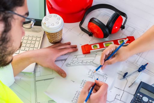 Two professional architects discussing a project on blueprints on the desk in an office