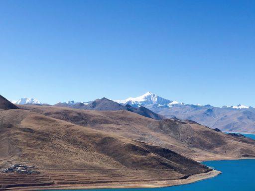 A scenic view of bare mountains along a river bank, against a clear blue sky