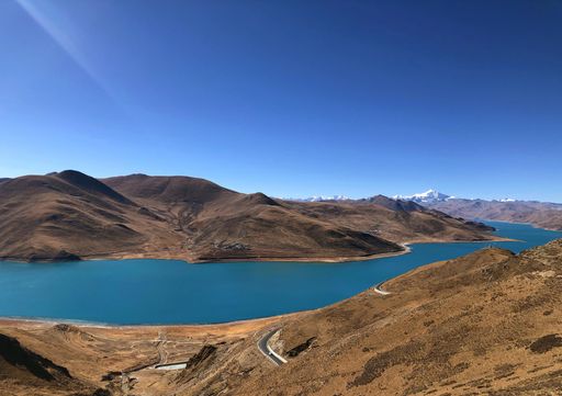 A scenic view of bare mountains along a river bank, against a clear blue sky