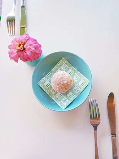 An overhead shot of a mini doughnut with forks, knives and flower on the white table