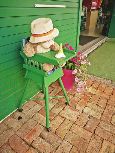 A vertical shot of a teddy bear on a chair against a wooden wall outside