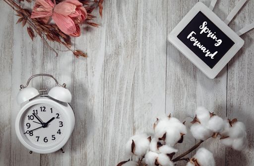 A top view pf an alarm clock and a small blackboard with a "Spring Forward" text on a wooden table