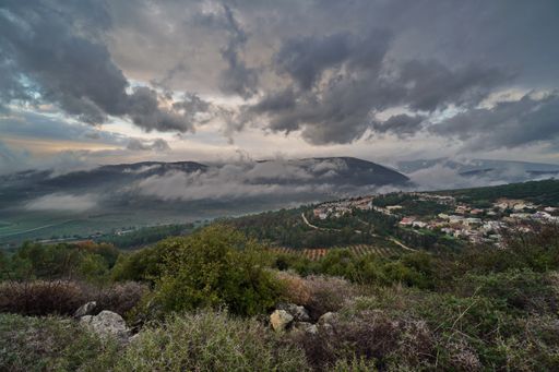 A landscape of hills covered in greenery and fog under a stormy sky in Lower Galilee, Israel
