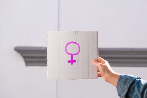 A woman's hand holding a cardboard with the pink female symbol