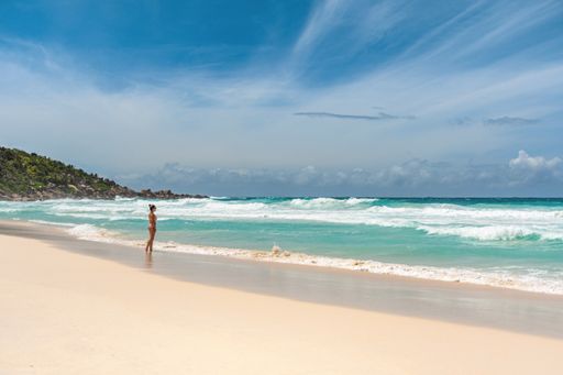Woman on beach with turquoise ocean and big waves on long tropical sandy beach on La Digue island on Seychelles.