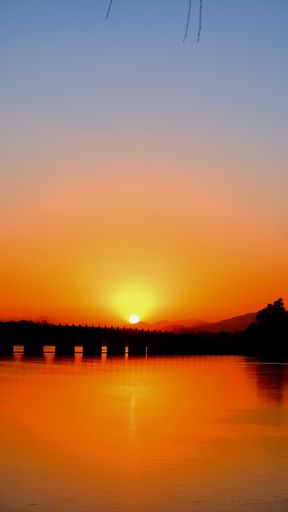 A vertical shot of a bridge over the river during sunset