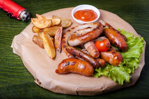 A closeup of grilled sausages with lettuce, fried potatoes, ketchup with green background