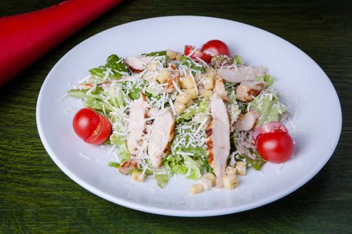 A closeup shot of tasty ceaser salad in a white plate with a green background