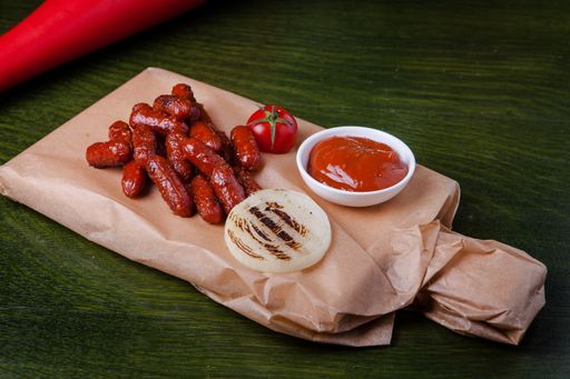 A closeup shot of grilled sausages with ketchup, tomato and fried onion on a chopping board