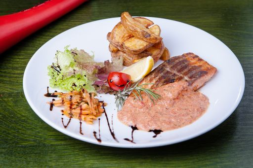 A closeup shot of a white plate filled with fried fish, vegetables and a sauce on a green table