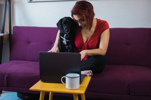 A closeup shot of a middle-aged female sitting with her dog and working in front of the laptop
