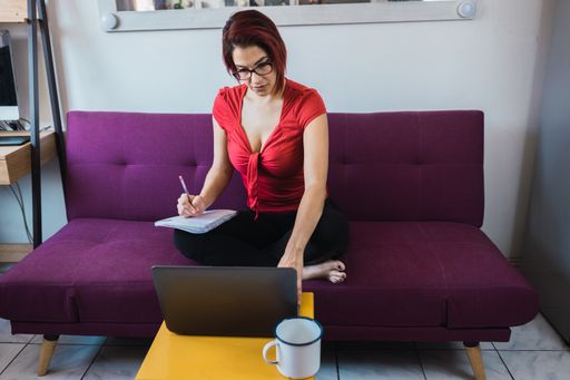 A middle-aged female working in front of the laptop with a notebook in her hands