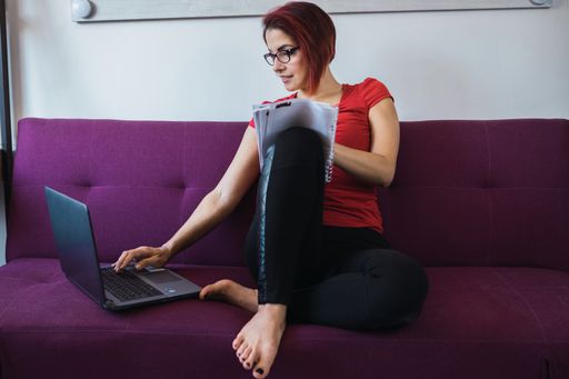 A closeup shot of a young beautiful woman writing and sitting on the sofa in front of the laptop