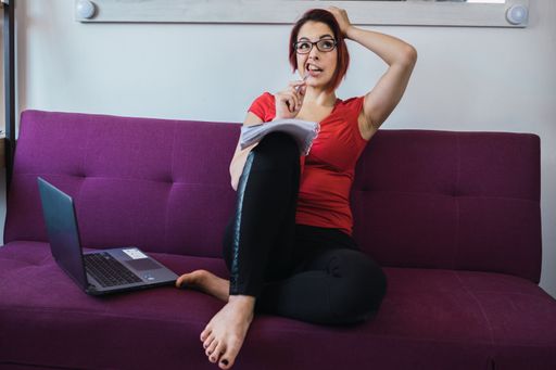 A middle-aged female working in front of the laptop with a notebook in her hands