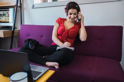 A closeup shot of a middle-aged female sitting with her dog and working in front of the laptop