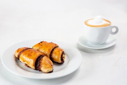 A closeup shot of delicious cinnamon croissant with cup of cappuccino