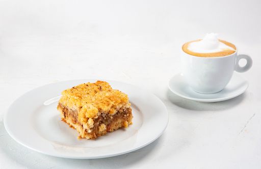 A closeup shot of a dessert plate near a cup of cappuccino isolated on white background
