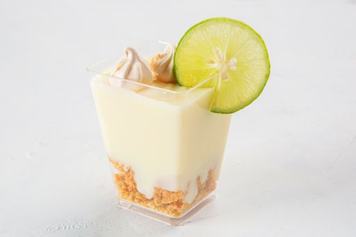 A closeup shot of lemon pie dessert with little meringues and a slice of lemon  on the top, served in a small plastic cup