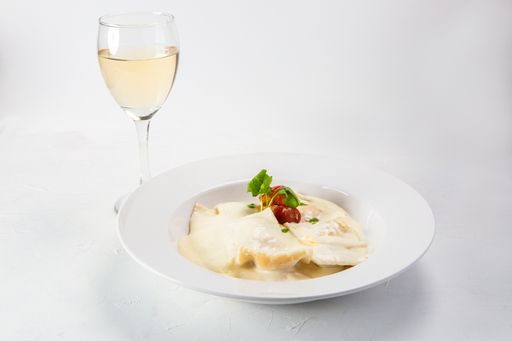 A closeup shot of delicious ravioli with sauce and a glass of wine on white background
