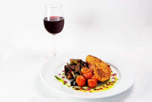 A closeup shot of a tasty looking dish near a wine glass isolated on white background