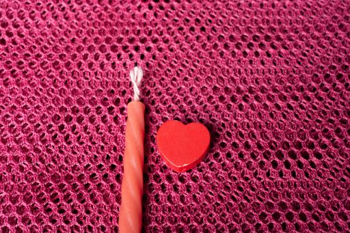 A high angle shot of a red candle and a heart-shaped object on a pink surface