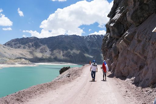 A group of people walking on a rural road towards high snowy mountains with the Chilean flag