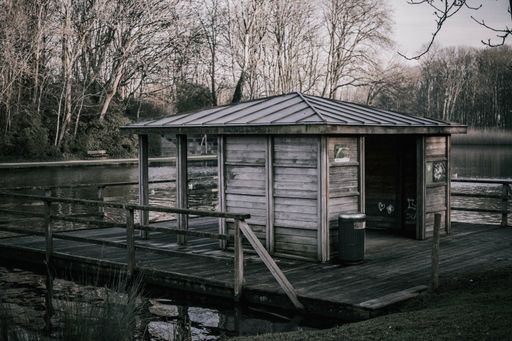 A closeup of an old wooden cabin over a lake surrounded by bare trees in the daylight