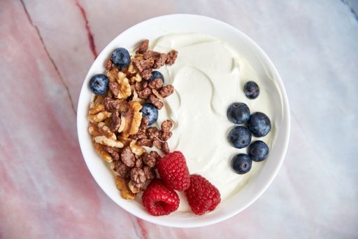A top view of a bowl with yogurt, raspberries, blueberries, walnuts, and cereals served on a table