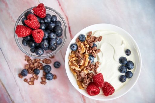 A closeup of a bowl with yogurt, raspberries, blueberries, walnuts, and cereals served on a table