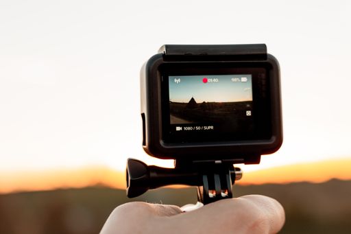 A closeup of a person's hand holding an action camera display recording the sunset in a meadow