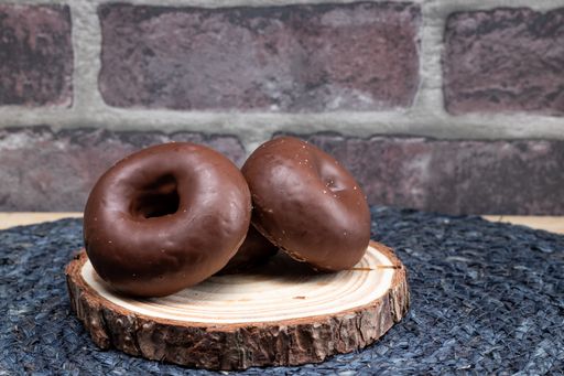 A couple of chocolate-covered donuts on a wood plate