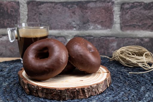 A couple of chocolate-covered donuts on a wood plate and a cup of coffee on the background