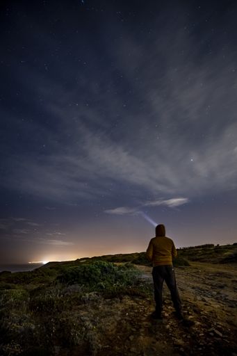 A vertical shot of a man standing on the rocks and looking at the shining stars in the night