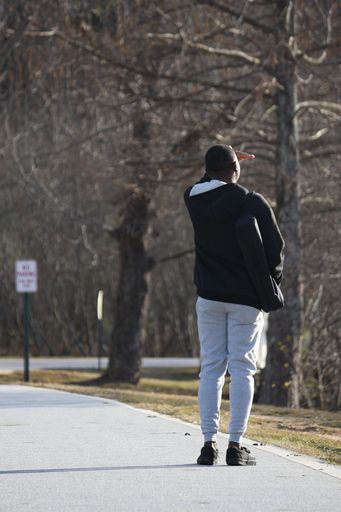 A rear view of a black guy in sportswear on a sunny street