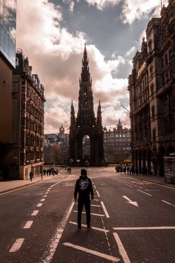 A vertical shot of a person standing in the middle of the road in front of the Scott Monument  in Edinburgh, Sotland