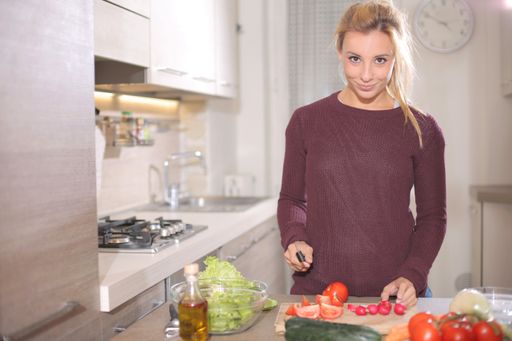 A young blonde female cutting vegetables in the kitchen under the lights